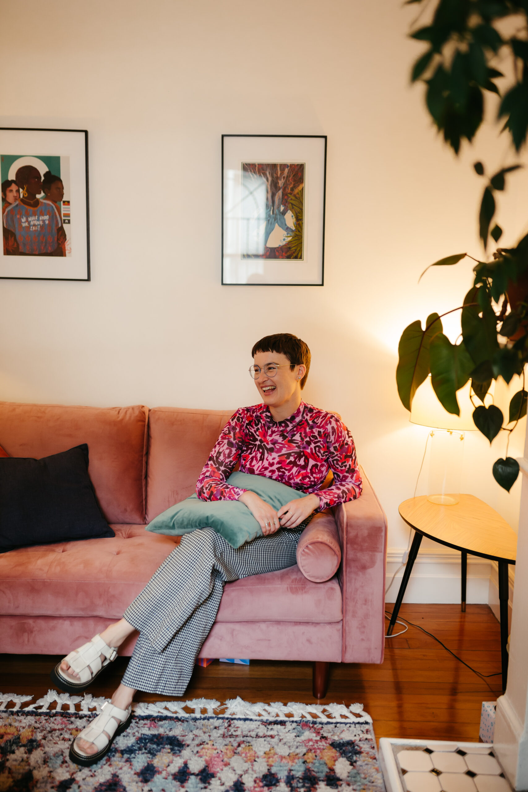 Chauncey Sjostedt laughing on a pink sofa in a room with plants and framed artwork